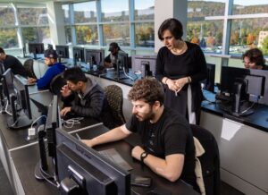 Prof. Nosrati stands behind a student working on a computer in the trading lab on campus.