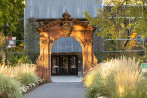 Havemeyer Arch in front of Academic Complex with tall grass and trees in foreground and an afternoon sunlight reflection.