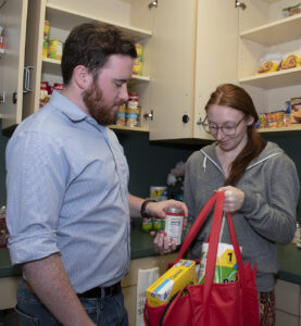 Asst. Director Dylan Heffernan assists a student with putting groceries in a bag in the on-campus food pantry.