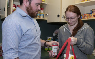 Asst. Director Dylan Heffernan assists a student with putting groceries in a bag in the on-campus food pantry.