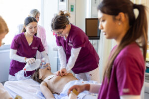 Ramapo College nursing students in maroon scrubs working on a simulated patient in the clinical lab on campus.