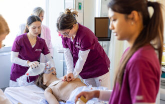 Ramapo College nursing students in maroon scrubs working on a simulated patient in the clinical lab on campus.