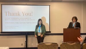 Emily stands at the podium and Dr. Dasgupta stands in front of a screen that projects the thank you slide from their research presentation.