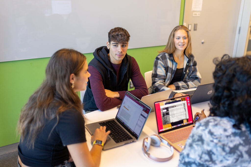 Three students sitting around a table with laptops working in a Learning Commons study room.