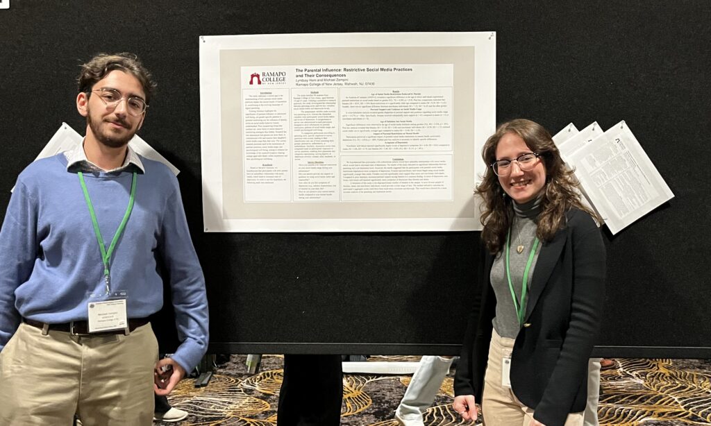 Michael Zampini ‘24 and Lyndsay Horn ‘24stand on either side of their research poster, which is pinned to a black board.