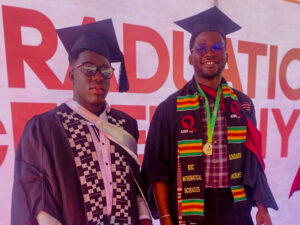 Two graduates stand side by side in black caps and gowns.