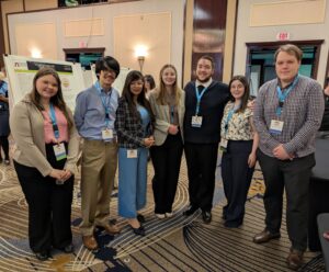 Dr. Dasgupta stands in front of a student research poster at the ECA conference. To the left of her is Sara Hosbach and Joseph Bennis To the right of her is Kaitlyn Camerlengo, Joseph Santana, Melissa Glasson, and William Jackson.