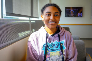 A female student wearing a lavender sweatshirt sits next to a window.