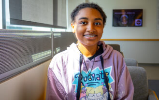 A female student wearing a lavender sweatshirt sits next to a window.