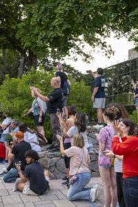 People stand on top of rock walls holding cameras. There are trees in the background.