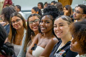 A group of three young women sit down and smile.