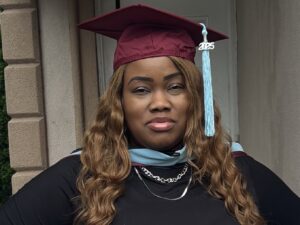 A woman with long brown hair wears a maroon mortar board hat with a light blue tassel.