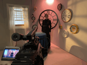 A video camera points toward a woman in a black dress.