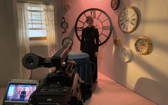 A video camera points toward a woman in a black dress.