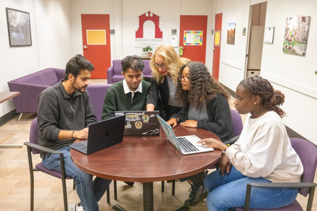 Students and a career center advisor gather around a table with laptops in the Cahill Career Development Center.