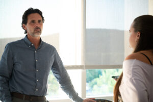 A man with a blue button down shirt stands up, listening to a college student speak.