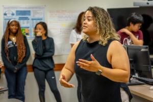 A woman with a black shirt engages with students in a classroom.