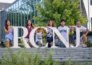 A group of six people pose outside with large letters, RCNJ.