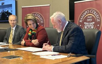 Three people sit behind a table to sign papers.