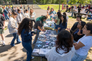 Students stand around a long table outside with papers on it.