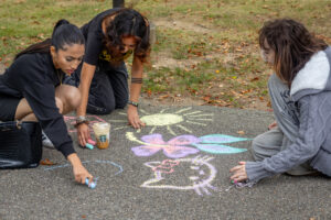 Three young women chalk a walkway.