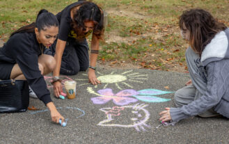 Three young women chalk a walkway.