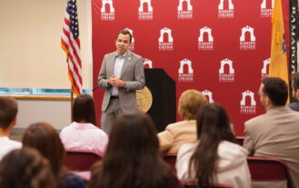 A man in a suit stands before a crowd and speaks.
