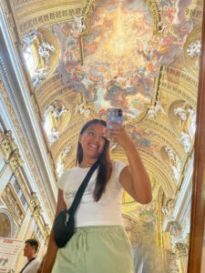 A young woman takes a selfie with a beautiful painted ceiling in the background. 