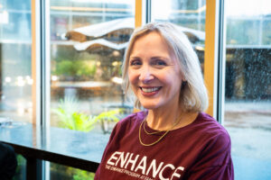 A woman wearing a maroon shirt smiles. She sits in front of a window.