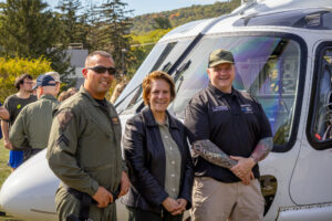 Three people stand in front of a helicopter.
