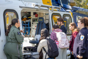 Five college students stand outside of a helicopter, looking inside. A flight nurse speaks to them.