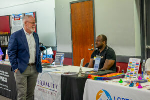 A man walks past a table where another man sits.