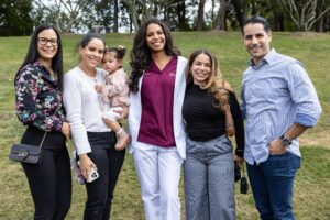 A group of people stand shoulder to shoulder, smiling. One holds a toddler.