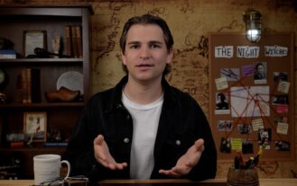 A man sits behind a desk with his hands open. He has a coffee cup on his desk, and a map in the background.