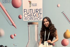 A woman stands behind a sign that reads, Future Chemist Workshop