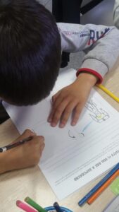 A student writes on a white piece of paper. The picture shows the top of his head, and his hands and the paper. 