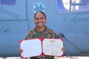 A woman in a military uniform holds a certificate and smiles.