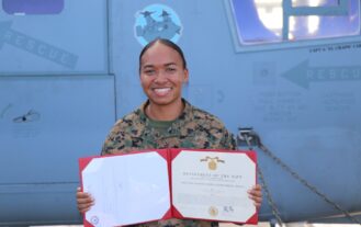 A woman in a military uniform holds a certificate and smiles.