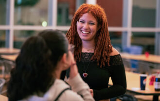 A woman in a black shirt smiles at another woman.