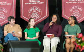 A group of thre people sit on a stage. One holds a microphone and the others listen.