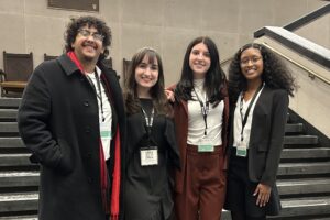 A group fo four college students stand shoulder to shoulder on steps outside.