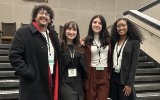 A group fo four college students stand shoulder to shoulder on steps outside.