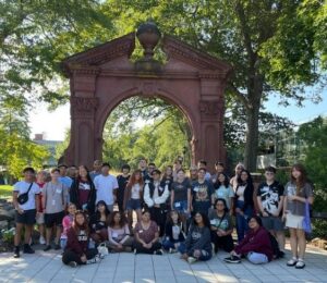 A large group of people gahter together in front of an arch outdoors.