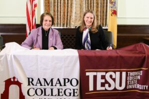 RCNJ President Cindy Jebb and TESU President Merodie Hancock sit side-by-side with their respective school banners draped on the dais for the LOI partnership signing.