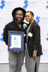 Lewis Spears is holding his award alongside the presenter in front of the Making A Difference Awards backdrop.