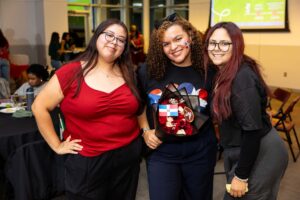 Three young women stand next to eachother and smile.