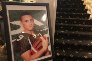 A large framed photo of a high school football player with a maroon jersey, holding a football, is poitioned next to a stairwell.