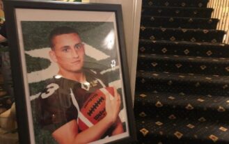 A large framed photo of a high school football player with a maroon jersey, holding a football, is poitioned next to a stairwell.