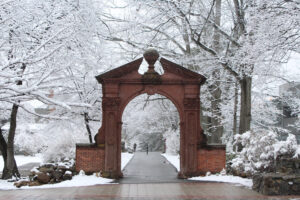 The Havemeyer Arch on the campus of Ramapo College is surrounded by trees with branches covered in snow.