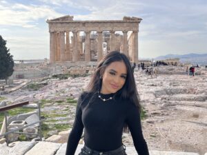 Woman with black shirt stands in front of historic ruins.